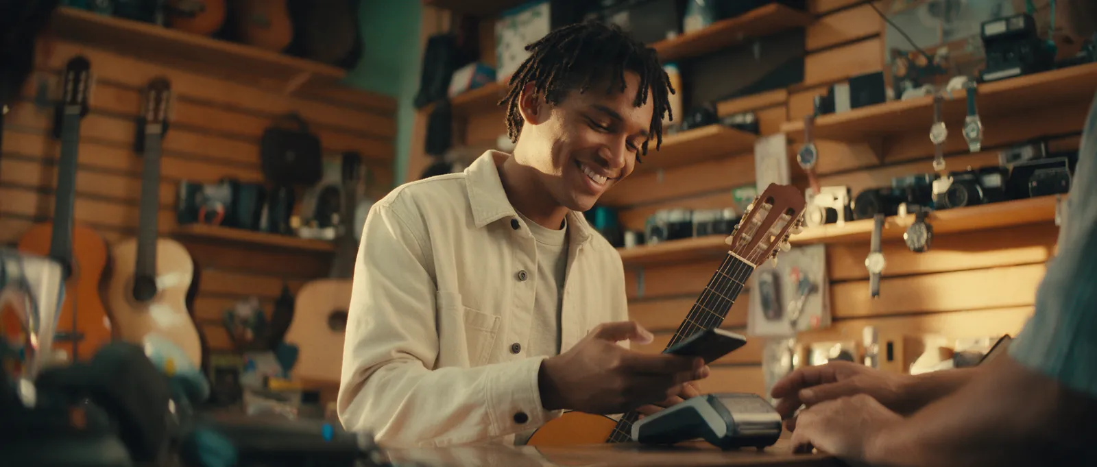 Joven pagando con su celular una guitarra en el mostrador de una tienda